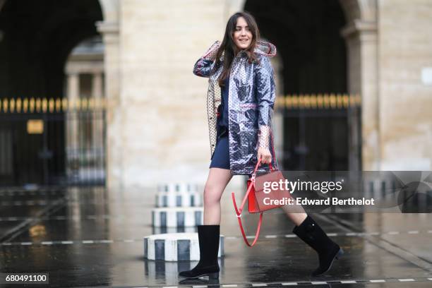 Sarah Benziane, fashion blogger, wears a Zara blue dress, a New Look clear plastic rain coat, an Ali Express red bag, and Chanel boots with flowers,...