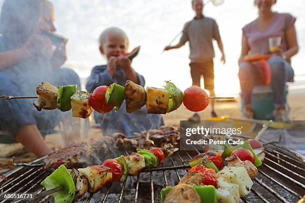 family having bbq on beach - bratspieß stock-fotos und bilder