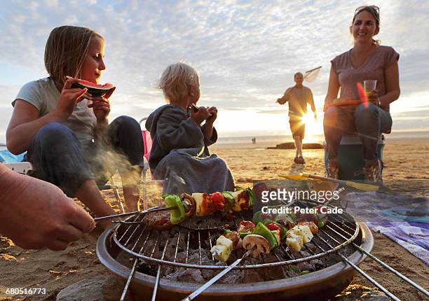 family having bbq on beach at sunset - barbecue cibo foto e immagini stock