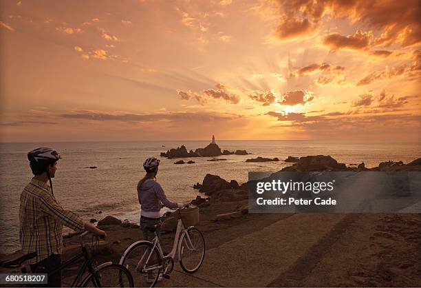 couple with bikes looking out to sea at sunset - jersey top stockfoto's en -beelden