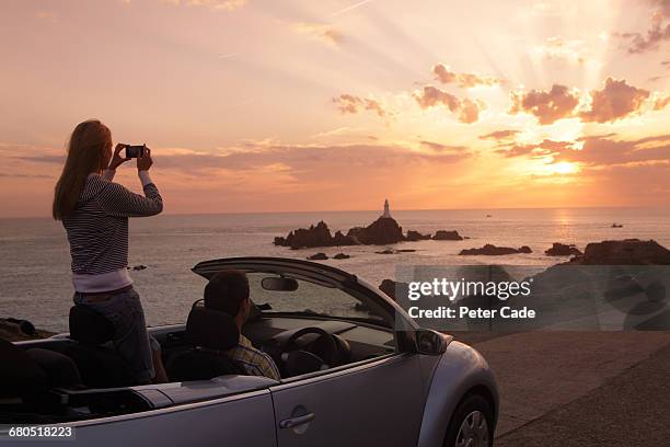 couple in car taking photo of coastal sunset - car top view foto e immagini stock