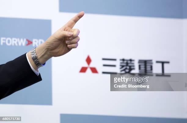 Shunichi Miyanaga, president and chief executive officer of Mitsubishi Heavy Industries Ltd., points as he speaks in front of the company's logo...