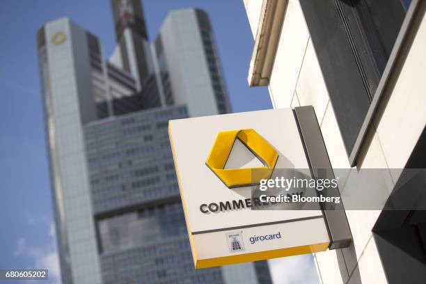 The Commerzbank AG logo sits outside a bank branch as the Commerzbank skyscraper headquarters stands beyond in Frankfurt, Germany, on Tuesday, May 9,...