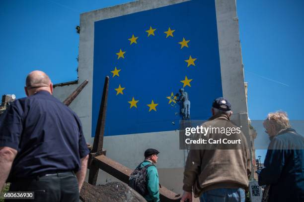 People view a recently painted mural by British graffiti artist Banksy, depicting a workman chipping away at one of the stars on a European Union...
