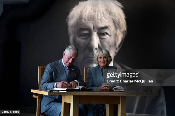 Prince Charles and the Duchess of Cornwall sign the visitors book as they visit the Seamus Heaney Home Place on May 9, 2017 in Bellaghy, Northern...