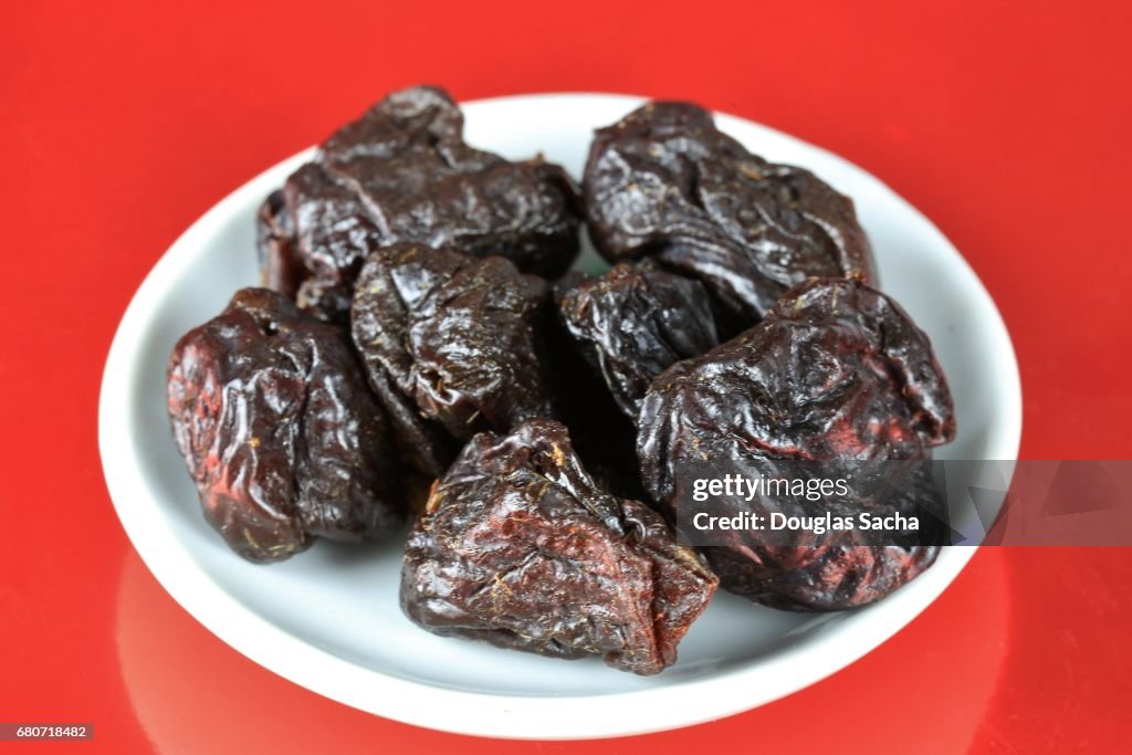 Serving dish of Dried Prunes on a red background (Prunus domestica)