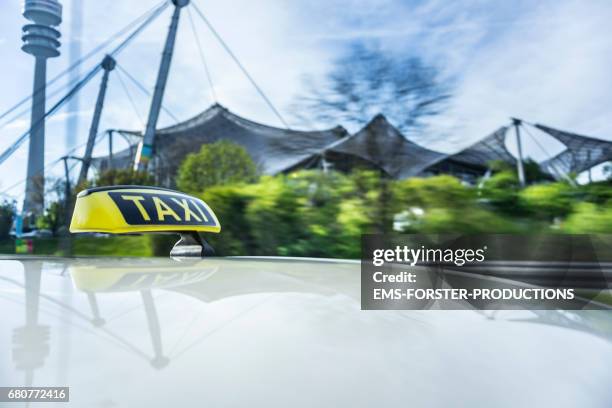 automotive on board a driving car long exposure rigging shot from the top of a german taxi. taxi roof sign / board / dachzeichen in foreground. reflections in the roofs surface of the yellow cab. in background, motion blurred and streaking the tv tower. - olympiastadion rasen stock-fotos und bilder