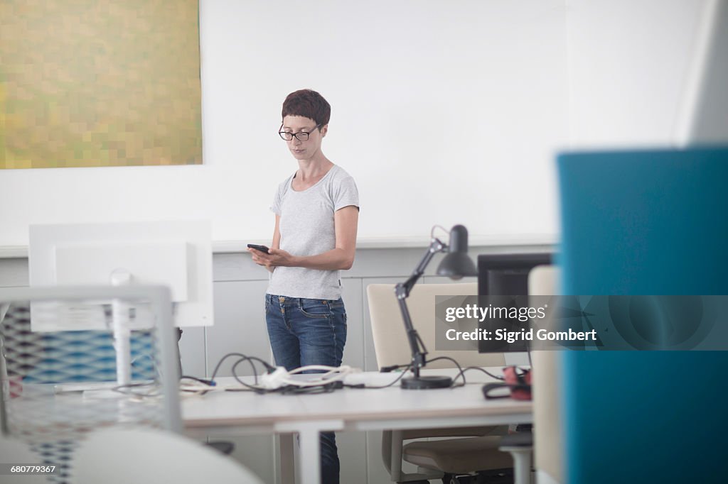 Mature woman text messaging on mobile phone in the office, Freiburg im Breisgau, Baden-Württemberg, Germany