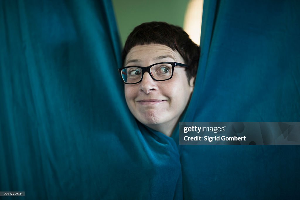 Mature woman peeking from curtain in the office, Freiburg im Breisgau, Baden-Württemberg, Germany