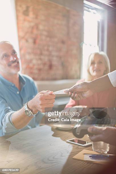 waiter with credit card reader giving man receipt at restaurant table - debit cards credit cards accepted stock pictures, royalty-free photos & images