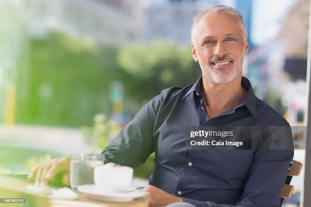 Portrait smiling man drinking coffee at urban sidewalk cafe