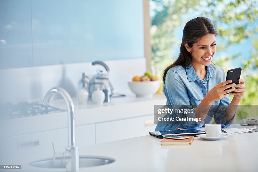 Smiling woman texting with cell phone at kitchen counter