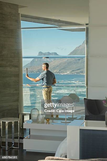 reflection of man using digital tablet camera on luxury balcony with ocean view - beach house balcony stock pictures, royalty-free photos & images