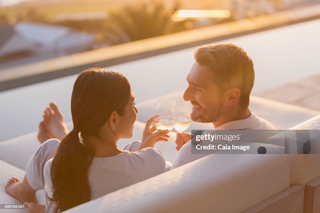 Couple relaxing toasting white wine glasses on chaise lounge on luxury patio