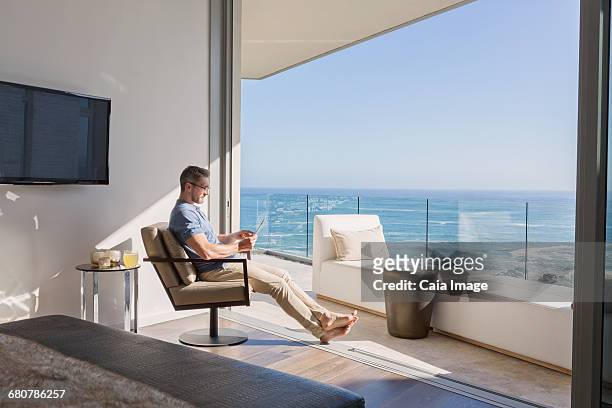 man using digital tablet overlooking sunny ocean view - beach house balcony fotografías e imágenes de stock