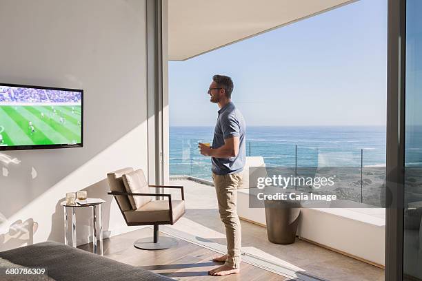 man watching soccer on tv at sunny luxury patio doorway with ocean view - beach house balcony stock pictures, royalty-free photos & images