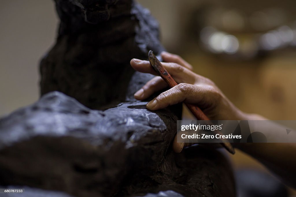 Cropped view of sculptor in artists studio creating sculpture with hand tool