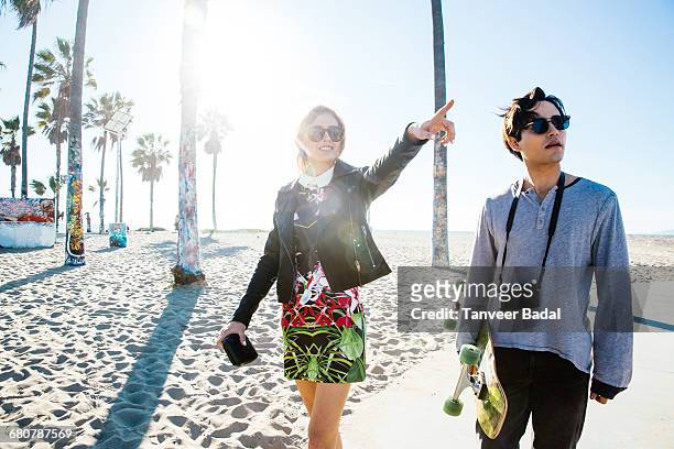 young couple walking along beach walkway, young woman pointing - venice couple foto e immagini stock