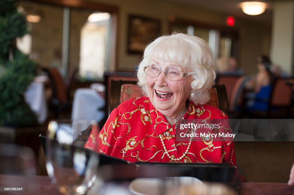 Senior woman sitting at table in restaurant, laughing