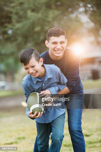 spanische teenager, bruder spielt fußball im park - two kids playing with hose stock-fotos und bilder