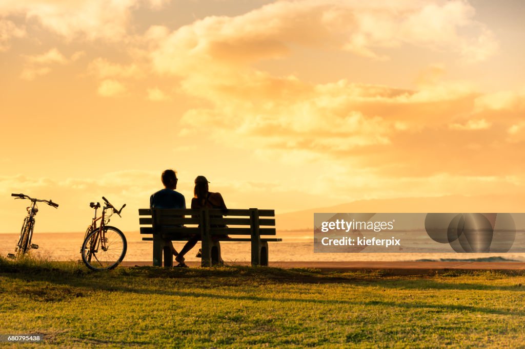 Couple sitting on park bench watching the sunset.
