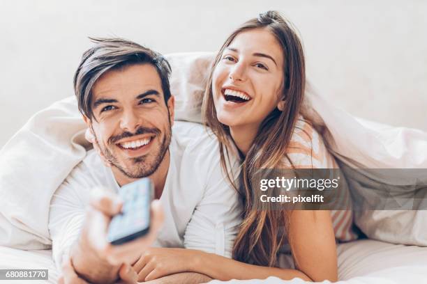 watching tv in the bed - young couple watching tv stock pictures, royalty-free photos & images