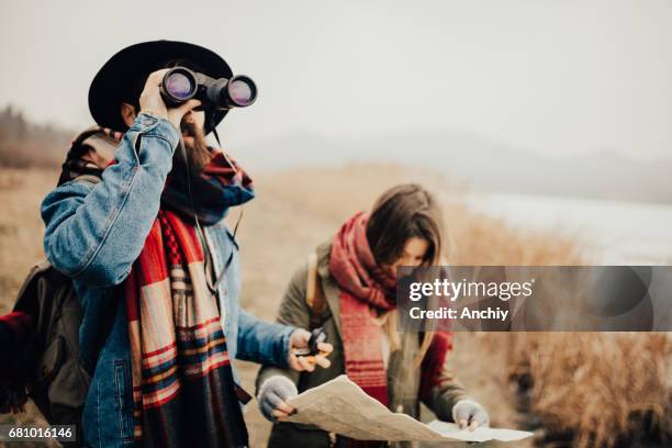 bearded hipster looking through binoculars while his friend is checking the map for directions - woman looking through ice stock pictures, royalty-free photos & images