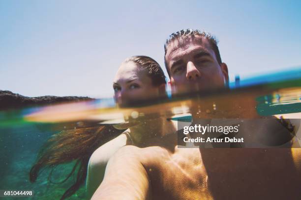 beautiful couple in love taking a selfie during travel vacations in tenerife island swimming in a stunning natural pool with clear and calm water and half underwater view. - standing water stock-fotos und bilder