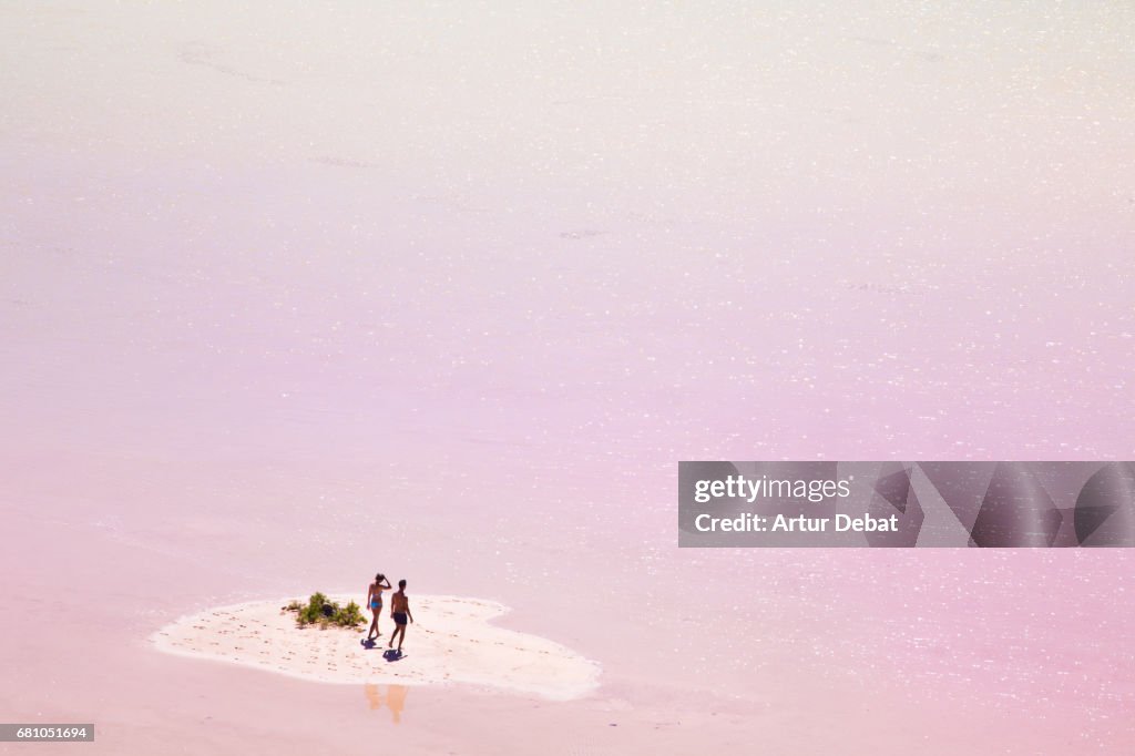 Stunning small island in the middle of the pink lagoon with couple enjoying the beach day in the Fuerteventura island during travel vacations.