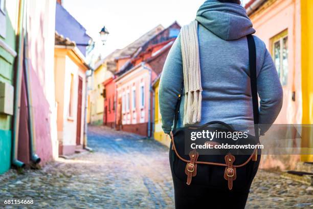 rückansicht des weiblichen reisenden tragen schwarze umhängetasche mit bunten häusern im hintergrund unscharf - camera bag stock-fotos und bilder