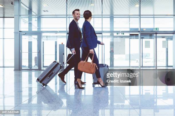 businesspeople walking with luggage inside airport terminal - couple traveler stock pictures, royalty-free photos & images