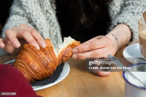 close up of female hands breaking off a piece of croissant in cafe. - medias lunas fotografías e imágenes de stock