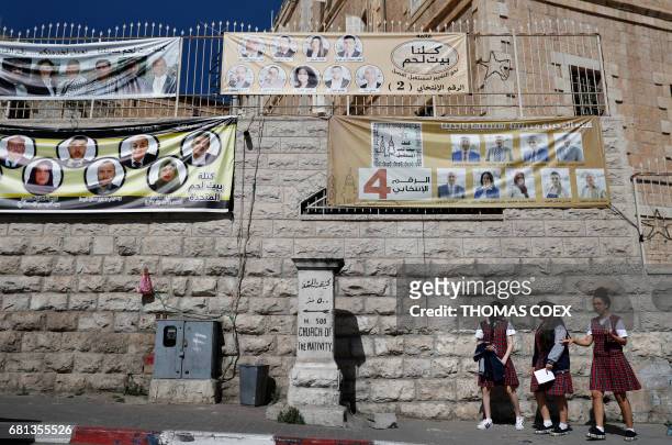 Palestinian schoolgirls walk past campaign posters displaying electoral lists ahead of municipal elections in the West Bank city of Bethlehem on May...