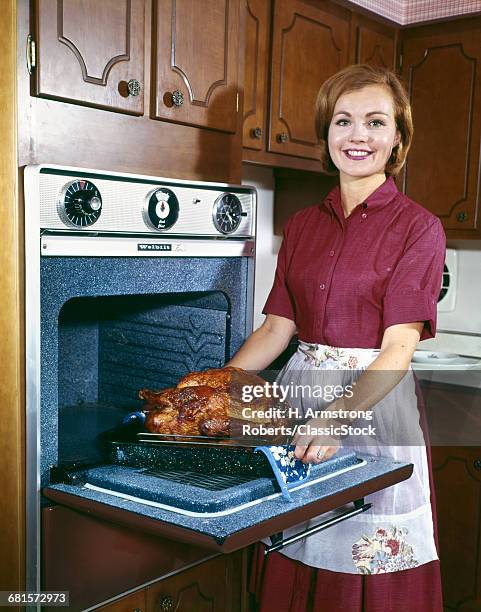 1960s SMILING WOMAN LOOKING AT CAMERA TAKING ROAST TURKEY OUT OF ELECTRIC OVEN