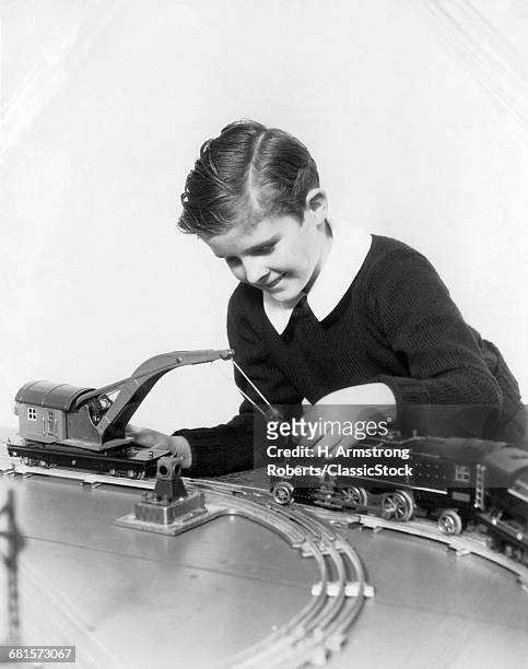 1930s SMILING BOY WEARING A SWEATER WITH WHITE SHIRT COLLAR PLAYING WITH CRANE CAR AND LOCOMOTIVE OF TOY TRAIN SET