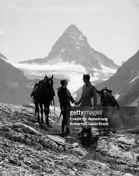 1920s 1930s COUPLE MAN WOMAN SILHOUETTED HOLDING HANDS STANDING WITH HORSES IN MOUNTAINS WESTERN MT. ASSINIBOINE CANADA