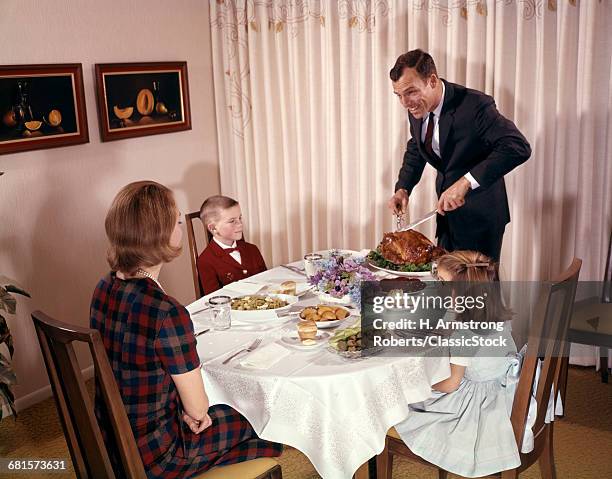 1960s FAMILY HOLIDAY DINNER FATHER CARVING TURKEY MOTHER BOY AND GIRL SEATED AT DINING ROOM TABLE