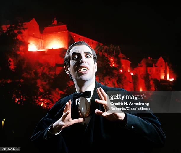 MAN IN VAMPIRE MAKEUP AND COSTUME GESTURING MENACINGLY CASTLE BACKGROUND LOOKING AT CAMERA