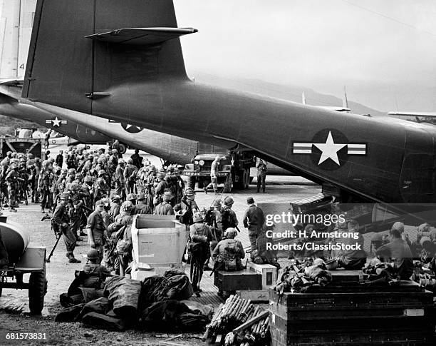 1960s MILITARY PERSONNEL GATHERED UNDER TAILS OF PLANES IN AIRFIELD WAITING TO BE AIRLIFTED FOR SPECIAL OPERATION IN VIETNAM