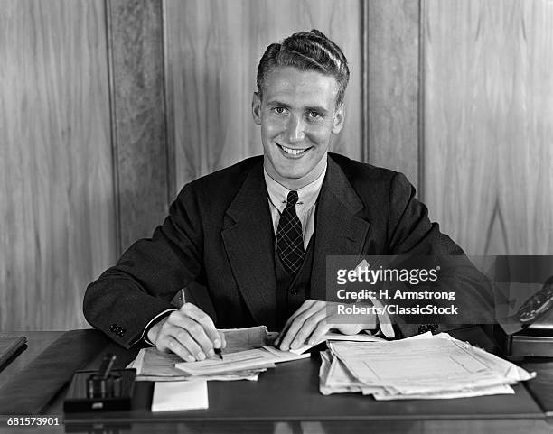 1930s 1940s SMILING BUSINESS MAN ABOUT TO SIGN A CHECK PEN IN HAND LOOKING AT CAMERA