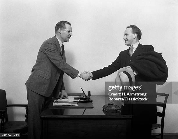 1930s TWO MEN SHAKING HANDS AT DESK IN OFFICE