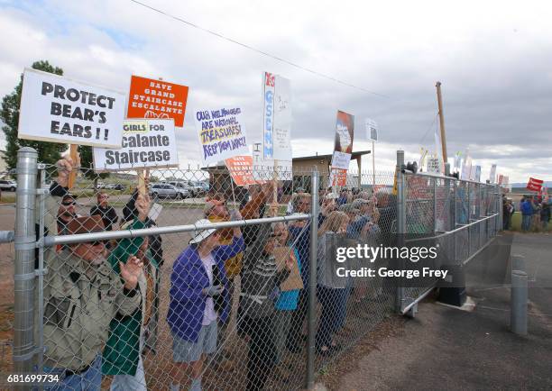 Protesters hold signs and chant behind a security fence as U.S. Secretary of the Interior Ryan Zinke arrives at Kanab Airport for departure on May...