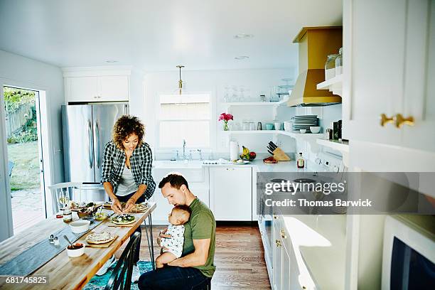 father holding infant while preparing dinner - cozy kitchen stockfoto's en -beelden