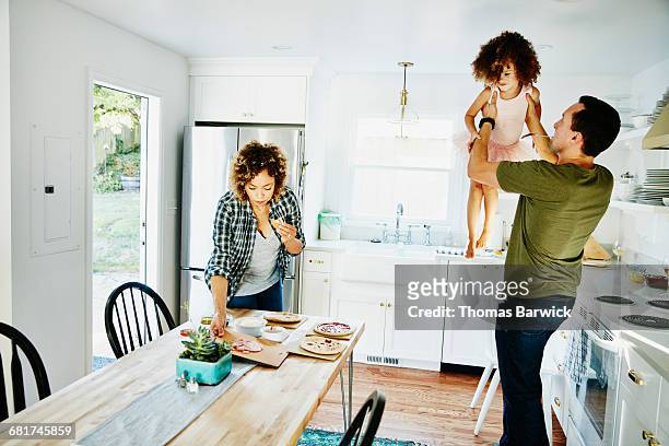 father lifting daughter in air in kitchen - leanintogether stock pictures, royalty-free photos & images