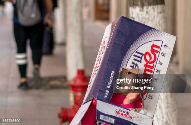 Little girl wearing a broken package box on head, playing on the street. According to a survey, the number of migrant children arrives at more than...