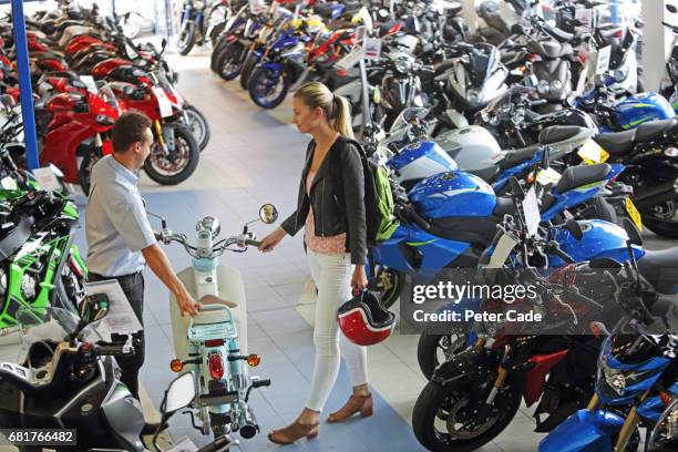 young woman talking to salesman in motorbike showroom - sold palabra en inglés fotografías e imágenes de stock