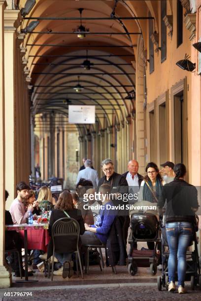 Pedestrians walk past people eating at a restaurant in the shade of one of the city's famous covered arcades alongside Via S. Felice on March 30,...