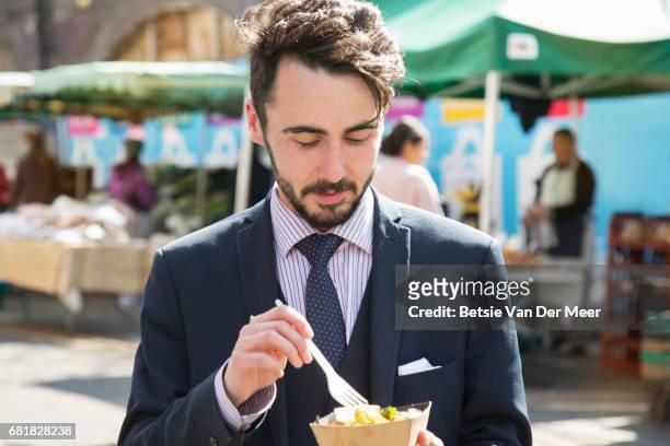 businessman eating street food, walking through urban food market. - eating on the move stock pictures, royalty-free photos & images