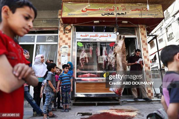 Syrian children watch as a butcher slaughters a camel in the rebel-held town of Douma, on the eastern outskirts of Damascus on May 11, 2017. Before...