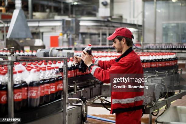 Worker places a bottle of Coke soda onto the automated bottling line at the Coca-Cola Hellenic Bottling Co. SA plant in Brovary, Ukraine, on...